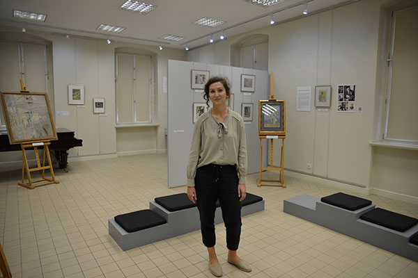 Fotografia przedstawia Martynę Wycisk, zastępcę dyrektora Muzeum Ziemi Kępińskiej. Młoda kobieta stoi na środku sali wystawienniczej. Za nią widoczne są obrazy. Autorem zdjęcia jest Dominik Wójcik.