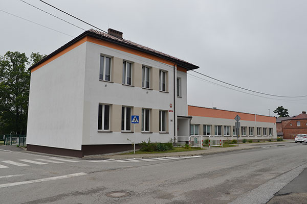 Fotografia przedstawia budynek szkoły podstawowej z oddziałami przedszkolnymi w Świbie. Budynek składa się z części dwu i jedno kondygnacyjnej, ma białą elewację. Autorem zdjęcia jest Dominik Wójcik.