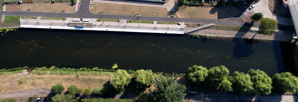 Fotografia z lotu ptaka przedstawia bulwary nad rzeką, płynącą przez mijscowość. Po obu stronach widać zabudowania mieszkalne oraz zagospodarowany brzeg. Zdjęcie pochodzi z archiwum beneficjenta.