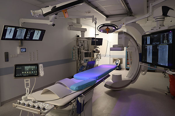 Na zdjęciu widzimy salę szpitalną wyposażoną w nowoczesny sprzęt. Jest łóżko nad którym przesuwa się półkolista część urządzenia. Wokół jest mnóstwo monitorów. Autorem zdjęcia jest Sebastian Mikołajczak.