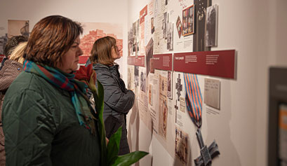 Na zdjęciu widzimy dwie kobiety – jedną na pierwszym planie, drugą na dalszym, które przyglądają się eksponatom na wystawie. Zdjęcie pochodzi z archiwum beneficjenta.