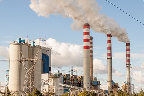 Na zdjęciu widzimy blok energetyczny elektrowni oraz cztery wysokie kominy, z których wydobywa się gęsty dym. Zdjęcie pochodzi z archiwum beneficjenta.