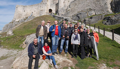 Na zdjęciu widoczna jest grupa ludzi, która pozuje na tle ruin zamku położonych na wzgórzu. Zdjęcie pochodzi z archiwum LGD Lider Zielonej Wielkopolski.
