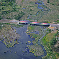 Fotografia z lotu ptaka przedstawia most biegnący na rozległym rozlewiskiem wodnym. Widoczne są nie tylko akweny, ale i porastające je roślinność. Zdjęcie pochodzi z archiwum beneficjenta.
