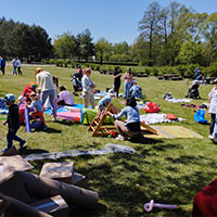 Zdjęcie przedstawia trwający piknik. Na trawie rozłożonych jest mnóstwo koców, wokół chodzą ludzie: dorośli i dzieci. Zdjęcie pochodzi z archiwum beneficjenta.