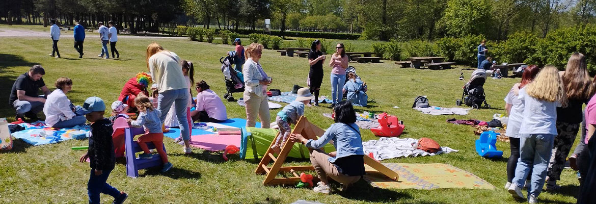 Zdjęcie przedstawia trwający piknik. Na trawie rozłożonych jest mnóstwo koców, wokół chodzą ludzie: dorośli i dzieci. Zdjęcie pochodzi z archiwum beneficjenta.