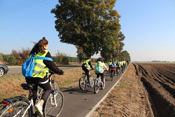 Zdjęcie ukazuje dużą grupę rowerzystów w odblaskowych kamizelkach, którzy poruszają się trasą rowerową. Zdjęcie pochodzi z archiwum beneficjenta.