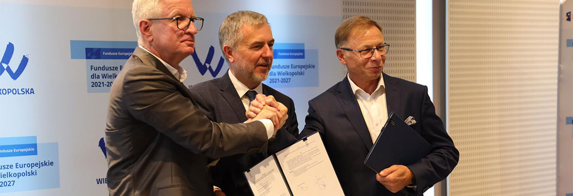 Na zdjęciu znajdują się trzej mężczyźni w garniturach, ściskający dłonie, prezentujący dokument. Fotografia pochodzi z archiwum Urzędu Marszałkowskiego Województwa Wielkopolskiego.