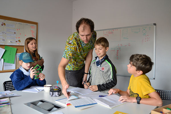 Fotografia przedstawia młodego nauczyciela, który tłumaczy coś trzem uczniom. Autorem zdjęcia jest Dominik Wójcik.