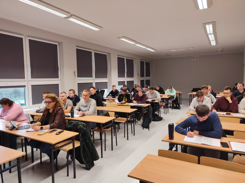 Na zdjęciu widoczni uczestnicy zajęć, siedzący w ławkach, w przestronnej sali. Fotografia pochodzi z archiwum beneficjenta.